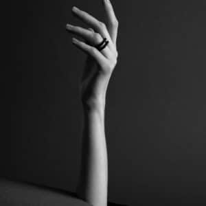 A hand wearing the DUALITY RING - MAKA on its middle finger reaches up through a circular hole in a flat surface. This bold black and white image offers unique inspiration for modern gift shop displays. Gate21.ee