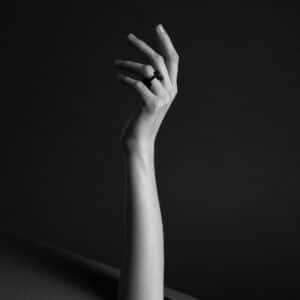 A single hand rises against a dark background, fingers gently curled, showcasing the DUALITY RING - KIMURA on the middle finger. Dramatic lighting highlights its elegant design, reflecting Tallinn shopping and unique local finds. Gate21.ee