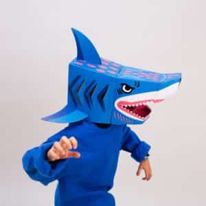 A person in a blue long-sleeve shirt poses with arms bent, wearing the Shark - 3D Mask, a vibrant cardboard costume. The playful look pops against the white background—ideal inspiration for a Tallinn concept shop display. Gate21.ee
