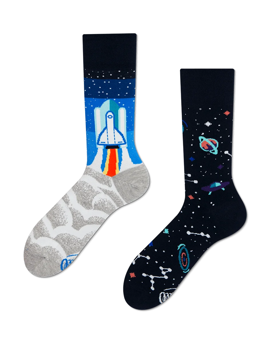 Two mismatched socks; one features a space shuttle launching with smoke and blue sky, the other displays a pattern of planets, stars, and constellations—curated in our gift shop for those seeking unique ideas. Gate21.ee