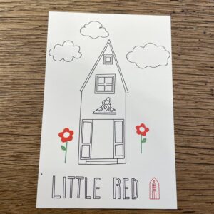 A postcard titled "Red House Colouring In" features a tall, narrow house with two red flowers, two clouds, and the words LITTLE RED at the bottom&mdash;an ideal Estonian souvenir from Tallinn, shown on a wooden surface. Gate21.ee