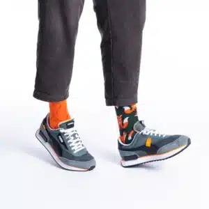 A person wearing dark grey corduroy trousers, orange and black fox-patterned socks, and grey and white trainers with orange accents—perfect for discovering unique ideas on your next Tallinn shopping adventure. Gate21.ee