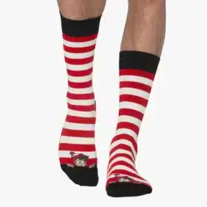 A person wears Wally - Regular socks with red and white stripes, black toes and cuffs, plus a small cartoon character with glasses and a matching hat near the toes—an Estonian-inspired Tallinn gift shop find. Gate21.ee