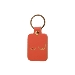 The Boob Key Ring - Coral is a rectangular orange leather keyring with a gold ring and an embossed line drawing of breasts—an Estonian-designed gift, ideal for those seeking something unique. Gate21.ee
