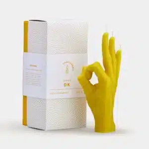 OK - Yellow is a candle shaped like a hand making the OK gesture in yellow, inspired by Estonian design. It comes next to a white, textured, gold-accented box—a unique addition to any concept shop or gift shop. Gate21.ee