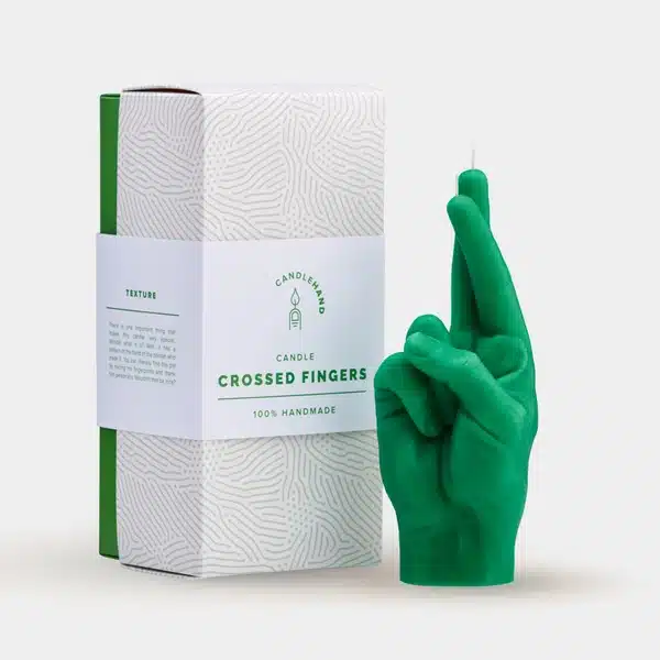 A green Fingers Crossed - Green candle, shaped like a hand with crossed fingers, stands by its box labelled 100% Handmade. Perfect for Tallinn shopping or curated gifts, it features a sleek white and green design. Gate21.ee