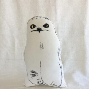 The Kakkud - Cushion - KÕIK is a white, owl-shaped pillow with minimalist black line art and yellow eyes, displayed upright against a light fabric background—an ideal choice for gift shops. Gate21.ee