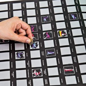 A hand scratches off a square on the Kama Sutra - Bucket List poster, revealing vibrant images beneath grey rectangles—an exciting gift or concept shop item to discover whilst shopping in Tallinn. Gate21.ee