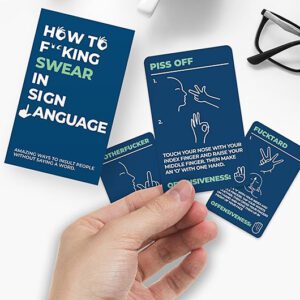 A hand holds a card from the “How to Swear in Sign Language - Card Game.” Two more cards and a booklet lie nearby—perfect for gifting or as a unique find on your next Tallinn shopping trip. Gate21.ee