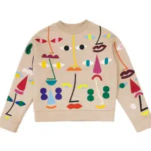 A beige jumper featuring a colourful abstract pattern of geometric shapes arranged to resemble various faces, inspired by curated, unique ideas from Tallinn shopping, with bold eyes, noses, and mouths across the front and sleeves. Gate21.ee