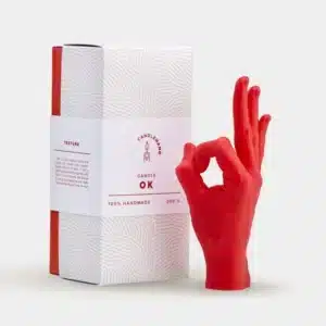 A red "OK" hand-shaped candle titled OK - Red stands beside a white box with textured patterns and red accents, exemplifying curated Estonian design from CANDLEHAND. Gate21.ee