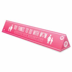 A pink triangular box labelled "100 Things to do with Mum - Bucket List," featuring woman and child icons, hearts, and scratch-off spots—an ideal Estonian design piece for concept stores or gift shops. Gate21.ee