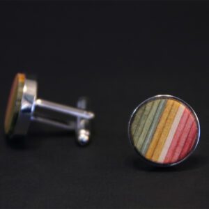 Triibuvineer cufflinks: round cufflinks with silver edges and a striped face in green, yellow, orange, and red on a dark background&mdash;unique accessories ideal for gifts or concept shops. One is upright while the other lies flat. Gate21.ee