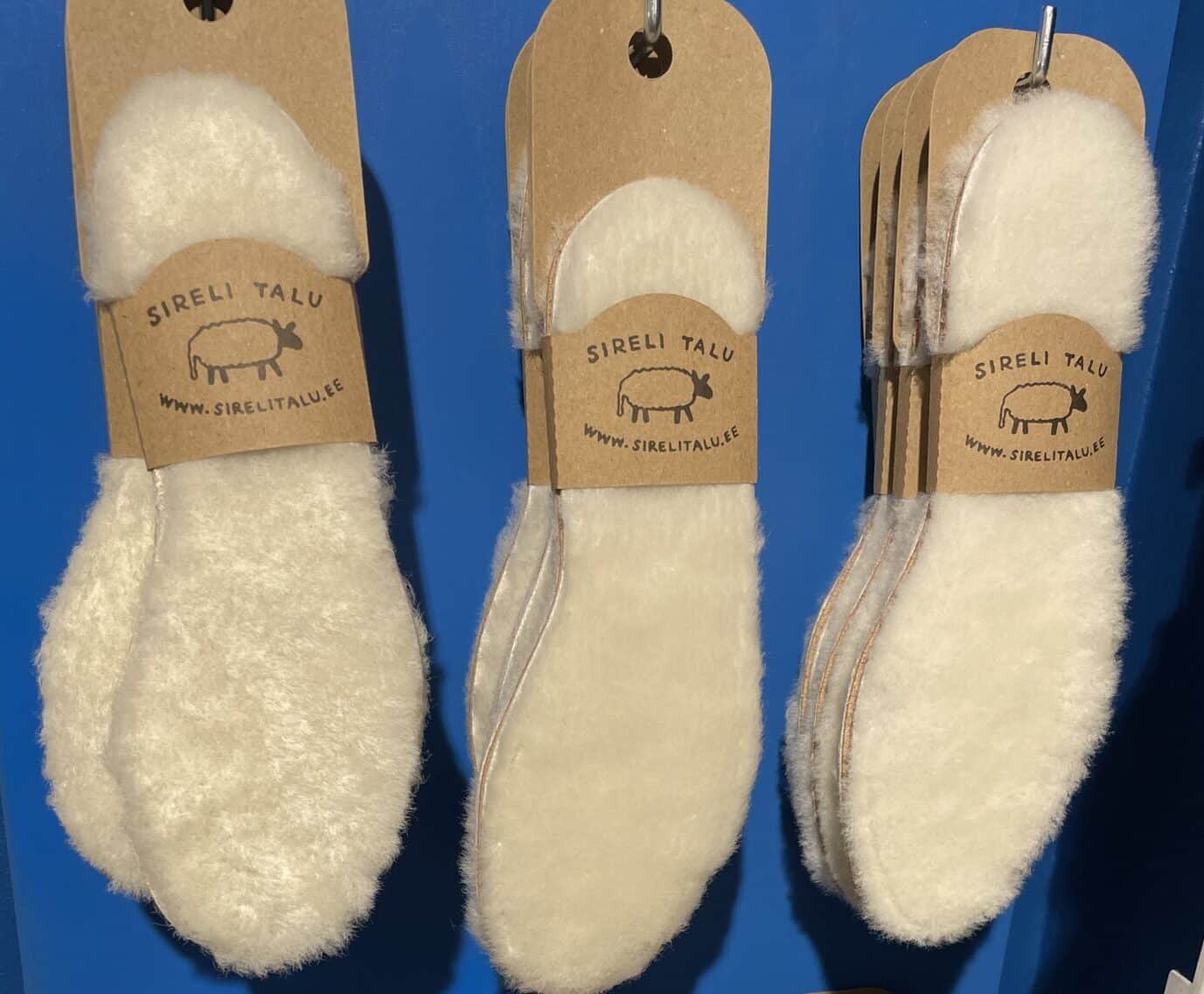 A set of Sheepskin Insoles - KÕIK from Sireli Talu, labelled with signature brown tags, is showcased against a blue background—ideal for concept shops or gift shops seeking unique display ideas. Gate21.ee