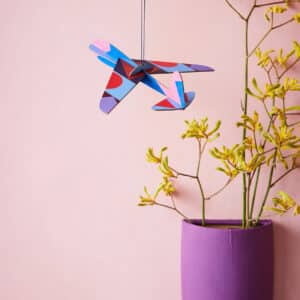 A Giant Glider Plane hangs from the ceiling near a wall-mounted purple vase with yellow-green flowers, set against a pale pink wall—perfect inspiration for your next Tallinn shopping concept store visit. Gate21.ee
