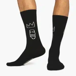 Someone wearing Basquiat Sugar Ray Robinson - Regular socks, featuring a white outlined crown and face design with “Market Lick” on the sole—an ideal gift shop find. Only their lower legs and feet are shown. Gate21.ee
