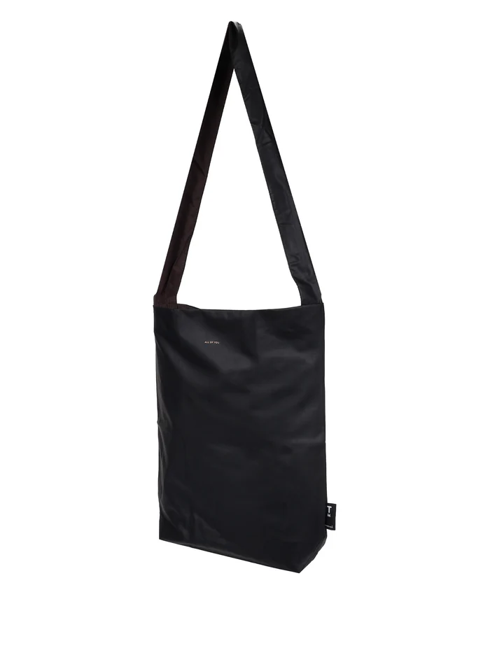 The Feel Good Bag - Black is a rectangular shoulder bag featuring a long strap, minimalistic design, and a small white logo near the top centre. Crafted in the signature style of Tinne+mia’s Feel Good Bag, it boasts smooth, slightly shiny material for an elegant finish. Gate21.ee