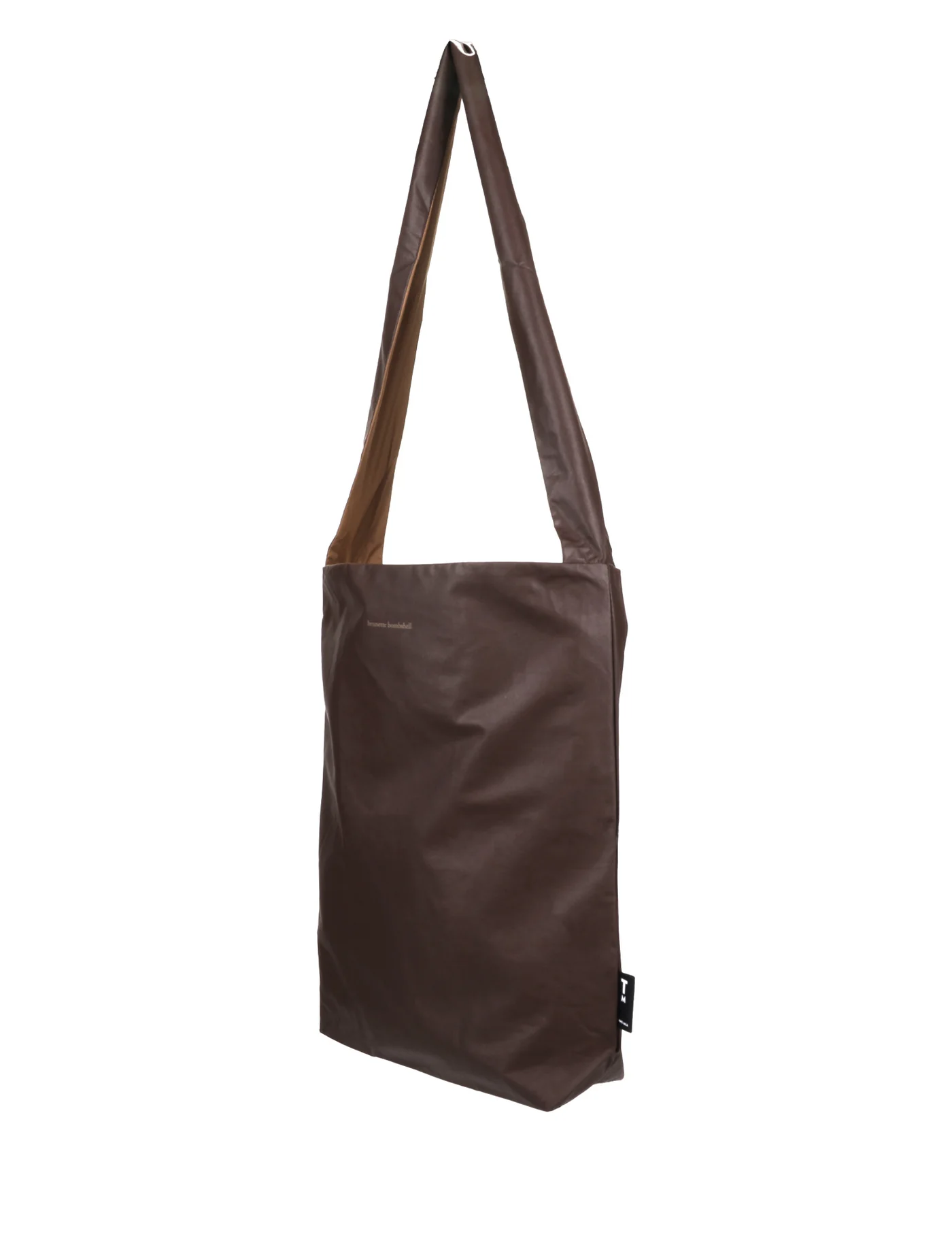 The Feel Good Bag - Chicory Coffee is a brown, rectangular Tinne+mia bag with a long strap, crafted from smooth leather-like material. Minimal detailing and a small black tag accent the lower right side. Gate21.ee