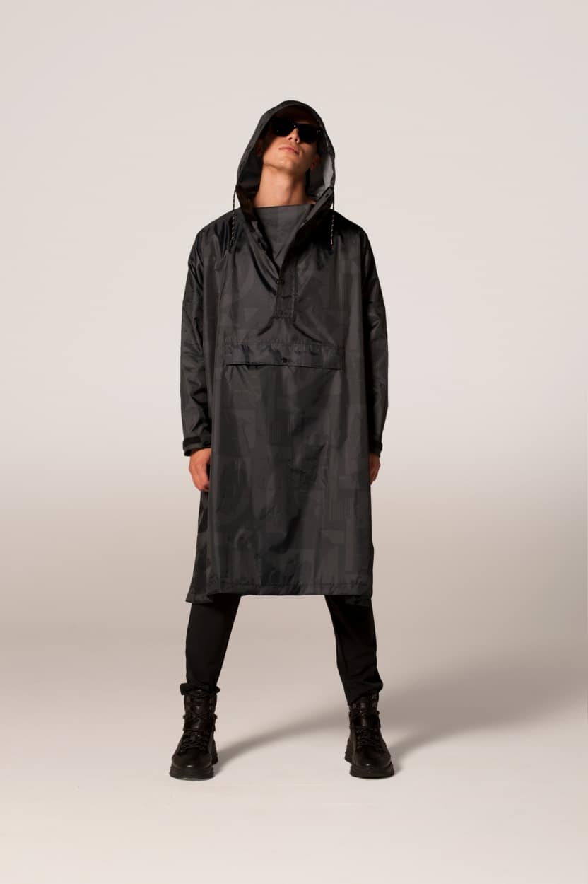 A person stands facing forwards in Back to Black—a long, black hooded raincoat—paired with black trousers, boots, and sunglasses against a neutral background; an ideal look for Tallinn shopping or browsing curated local gifts. Gate21.ee