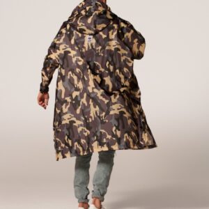 A person stands with their back to the camera, wearing the camo coat featuring a long, hooded, camouflage pattern inspired by Estonian design, paired with light grey trousers and white trainers against a plain background. Gate21.ee