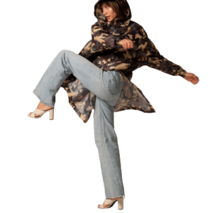 Wearing the "Camo" hooded jacket, light blue jeans, and white heeled sandals, a person strikes a pose with one leg raised against a plain white background. Gate21.ee