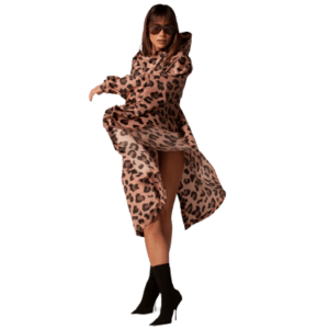 A woman in the Pink Panther long, flowing leopard print coat, black high-heeled boots, and sunglasses poses with one leg raised against a white background, embodying the bold spirit of curated Estonian design. Gate21.ee