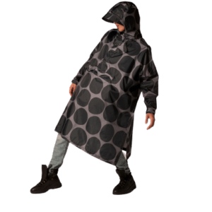 A person models the Polka black hooded rain poncho with large grey polka dots, paired with light trousers and black boots against a white background—ideal for a curated concept shop or stylish gift shop display. Gate21.ee
