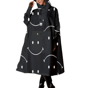 A woman models the Digi Spring black hooded rain poncho, featuring white smiley faces inspired by Estonian design, paired with black heeled boots against a plain white background. Gate21.ee