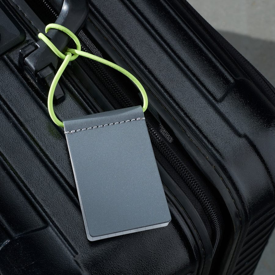 A black hard-shell suitcase features the Luggage Tag - Neon Yellow in close-up, attached by a bright yellow-green loop. Sleek and modern, the tag shows no visible writing or logo&mdash;ideal for your next Tallinn shopping spree or local concept shop find. Gate21.ee