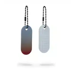 Two oval-shaped metal keyrings hang side by side on ball chains. The Reflective Tag – Red Fade boasts a grey surface with a red edge, standing out against a crisp white background—perfect for gift shops or concept stores. Gate21.ee