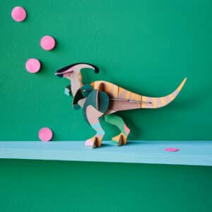 A vibrant cardboard Parasaurolophus dinosaur model sits on a light blue shelf against a green wall with pink paper circles—perfect decor inspiration from Tallinn’s top concept stores or gift shops. Gate21.ee
