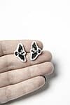 A hand displays the Lendavad varesed Kõrvarõngad—black and white butterfly-shaped earrings—against a plain white background, highlighting their unique Estonian design. Perfect as a gift or stylish addition from a curated concept shop. Gate21.ee