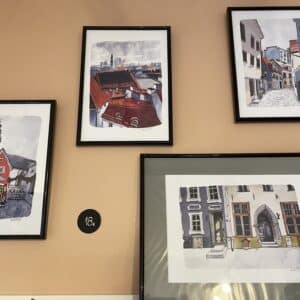Four OlevusArt Old Town Posters - K&Otilde;IK featuring European city scenes decorate a beige wall&mdash;three vertical, one large horizontal&mdash;showcasing unique urban architecture, ideal for those seeking Tallinn shopping inspiration or concept store display ideas. Gate21.ee