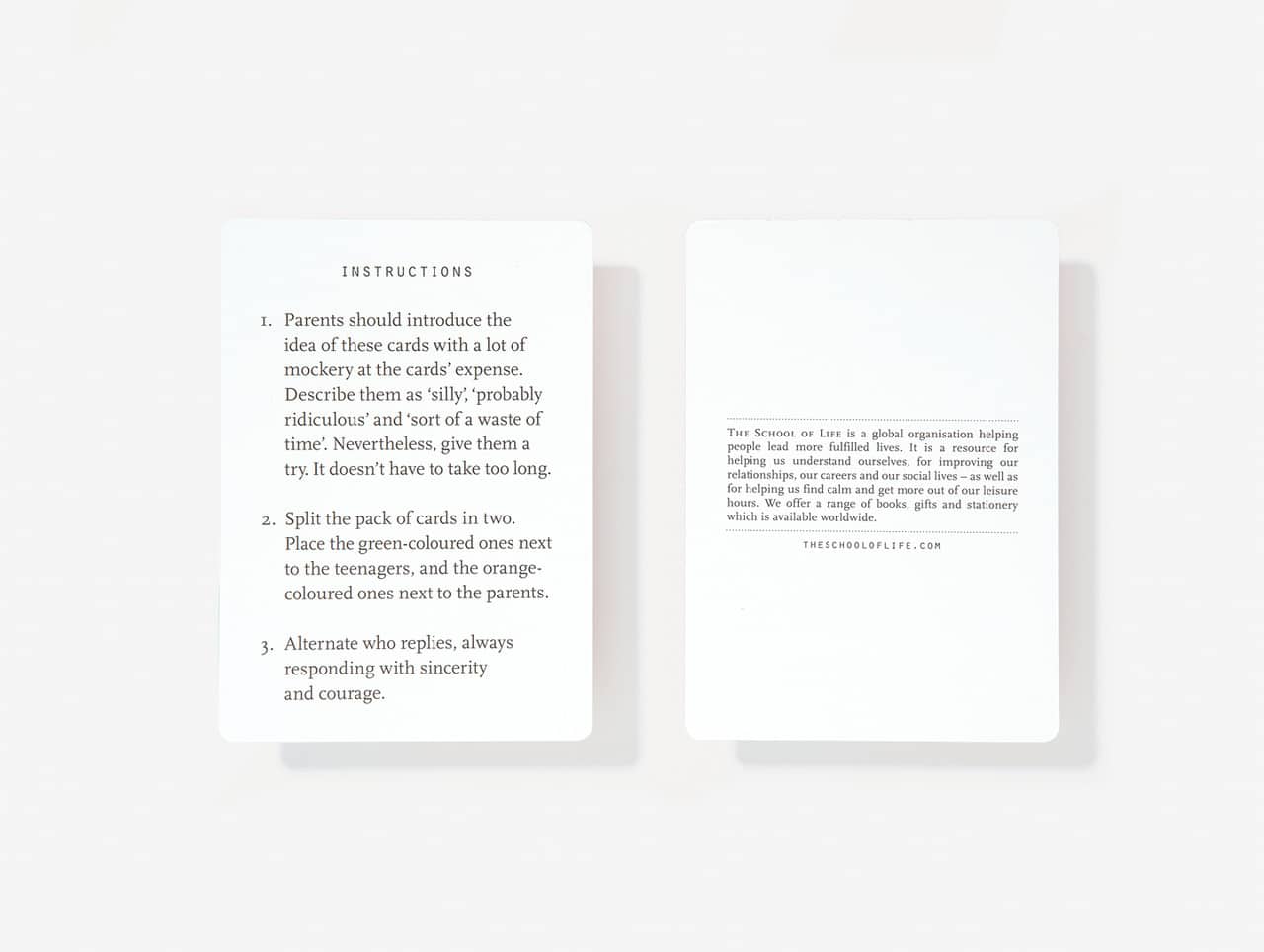 Two white cards from the Parents & Teenagers Game are displayed on a flat surface. The left card shows game instructions, whilst the right features printed text with a website URL. Both cards have a clean, minimal Estonian design that highlights unique ideas. Gate21.ee