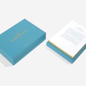 A blue box labelled Parents & Teenagers Game sits closed next to an open box with a stack of printed papers, each curated with unique ideas and featuring touches of Estonian design, all arranged on a white surface. Gate21.ee