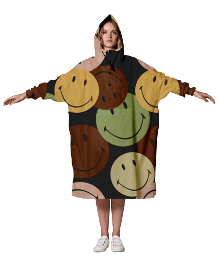 A person wears the Retro Smiley hooded oversized blanket featuring large brown, green, yellow, and tan smiley faces—arms outstretched against a plain background; ideal for any curated gift shop or concept store collection. Gate21.ee