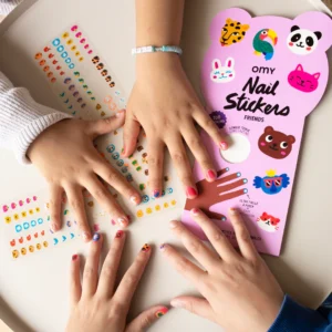Three children&rsquo;s hands with colourful animal-themed Friends - Nail Stickers from OMY are shown around a table, along with a pink sheet labelled &ldquo;Nail Stickers&rdquo; and a sticker sheet displaying small icons. Gate21.ee