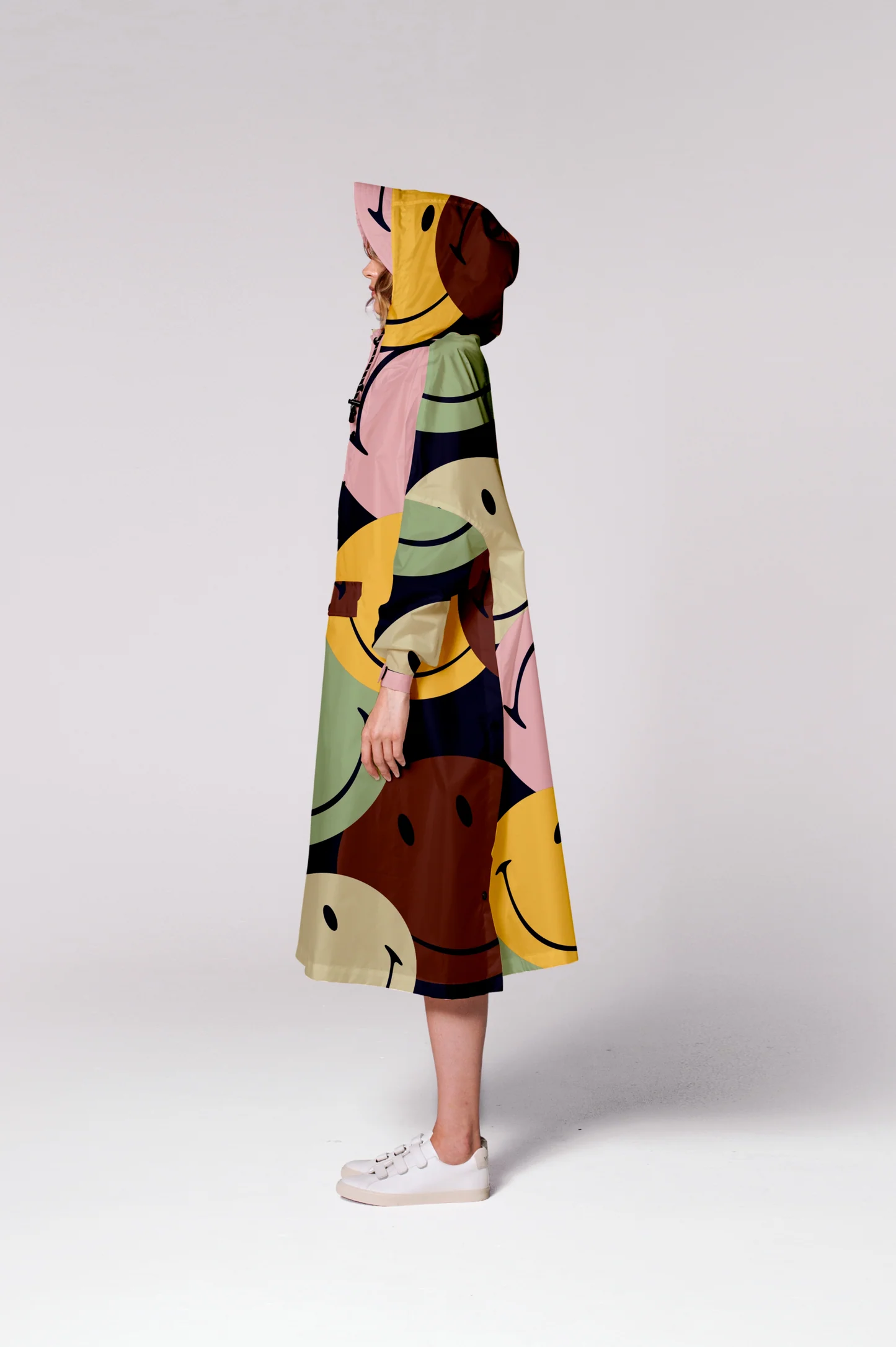 Model stands in profile wearing the Retro Smiley hooded, long-sleeve dress featuring a vibrant, overlapping smiley face pattern, paired with white trainers against a plain background—perfect for brightening up Tallinn shopping days. Gate21.ee