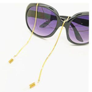 A pair of black sunglasses with purple-tinted lenses, featuring a gold spectacle chain attached to both arms, rests on a white surface&mdash;a perfect find for Tallinn shopping or lovers of Estonian design. Gate21.ee