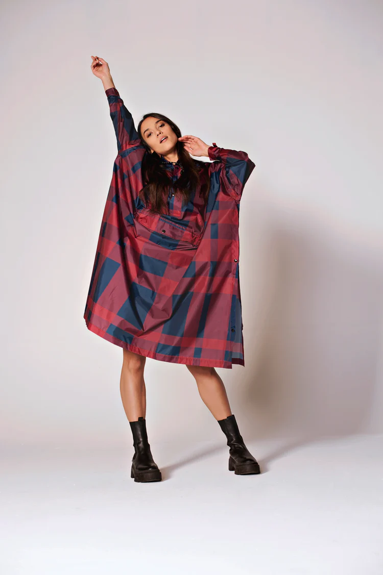 A woman models Jasper, a loose, oversized red and navy checked dress, standing against a plain backdrop with one arm raised. She completes her look with black chunky boots—perfect for curated concept shop visits. Gate21.ee