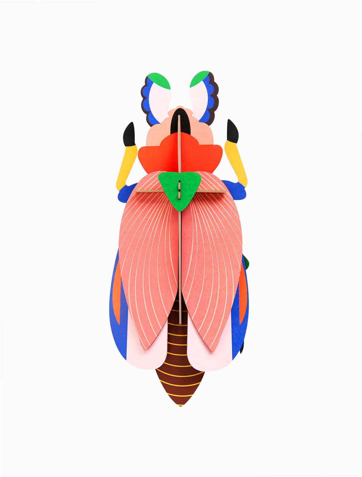 The Giant Ladybird is a colourful geometric paper sculpture with pink wings, a green triangle at the top, yellow legs, and blue, brown, and black accents—a striking piece for any concept shop seeking unique decor. Gate21.ee