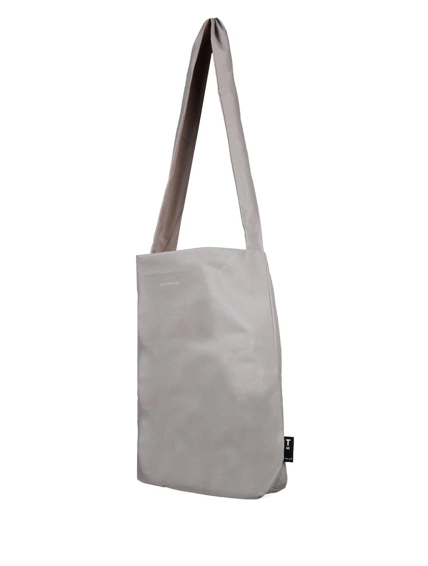 The Feel Good Bag - Feather Grey by Tinne+mia is a plain light grey shoulder bag with a long, wide strap and rectangular shape, shown against a white background. It features a small black tag on the side. Gate21.ee