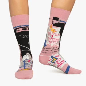 A person wears Basquiat Six Fifty - Regular crew socks with vibrant abstract faces, text, and anatomical art. Featuring pink cuffs, heels, and toes on a white base, they're perfect for gift shops or concept stores seeking unique socks. Gate21.ee