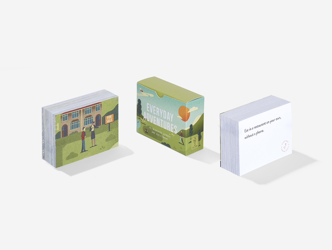 Three stacks of Everyday Adventures Cards are displayed side by side: the left shows people in front of a building, reflecting curated Estonian design; the middle features a green Everyday Adventures Cards box; the right stack displays a card with printed text. Gate21.ee
