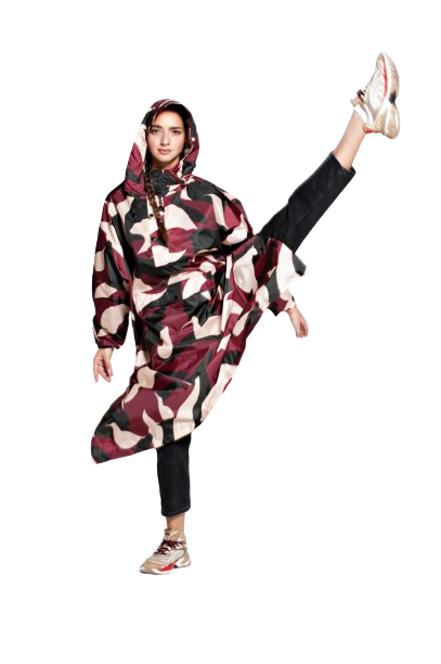 Wearing the Animo Bordeaux hooded oversized poncho, featuring a maroon, black, and white abstract Estonian design, a person balances on one leg with the other lifted high—styled with black trousers and trainers. Gate21.ee