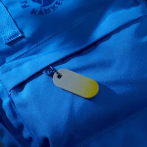 A close-up of a blue Kånken backpack shows a front zip pocket with a Reflective Tag - Yellow Fade keyring attached to the zip pull, adding a touch of curated Estonian design to this everyday essential. Gate21.ee