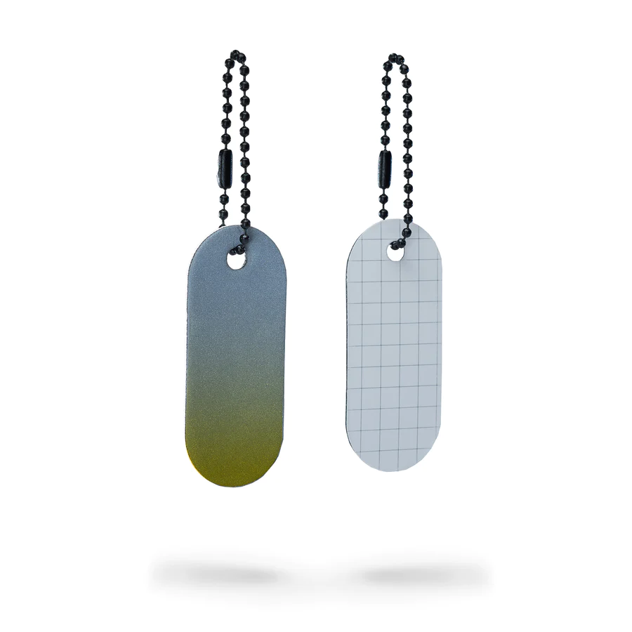 The Reflective Tag - Yellow Fade is an oval-shaped metal tag with a grey-to-yellow gradient and a ball chain. Ideal for Tallinn shopping or as a unique gift shop find, it has a hole at the top to attach the chain. Gate21.ee