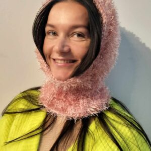A woman in a vibrant yellow outfit and a textured, light pink Riivo hat smiles at the camera, her curated style ideal for showcasing Riivo - Hats against a plain light grey background, perfect for concept shops or gift shops. Gate21.ee