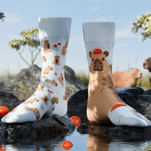Capybara socks, featuring capybara and orange designs, are shown on rocks in shallow water with sliced oranges nearby. Inspired by Estonian nature, these unique socks make a standout display for gift shops or concept stores. Gate21.ee