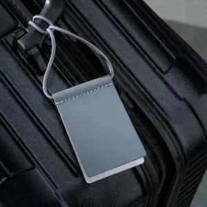A close-up of a black hard-shell suitcase with the Luggage Tag - Silver, an Estonian-designed tag featuring white stitching and blank lines for personalisation, adding distinctive style to your travel essentials. Gate21.ee